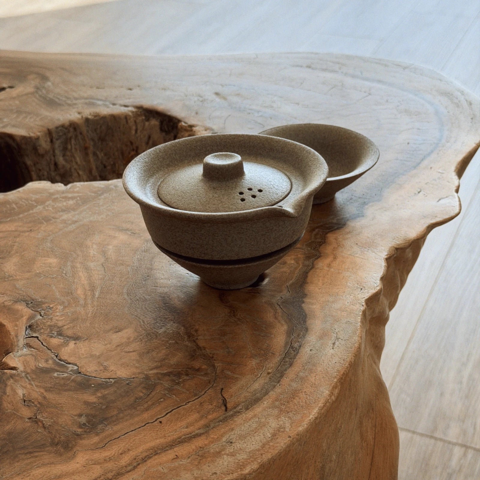 Beige ceramic gaiwan with lid and two cups arranged on natural wood slab, top angle