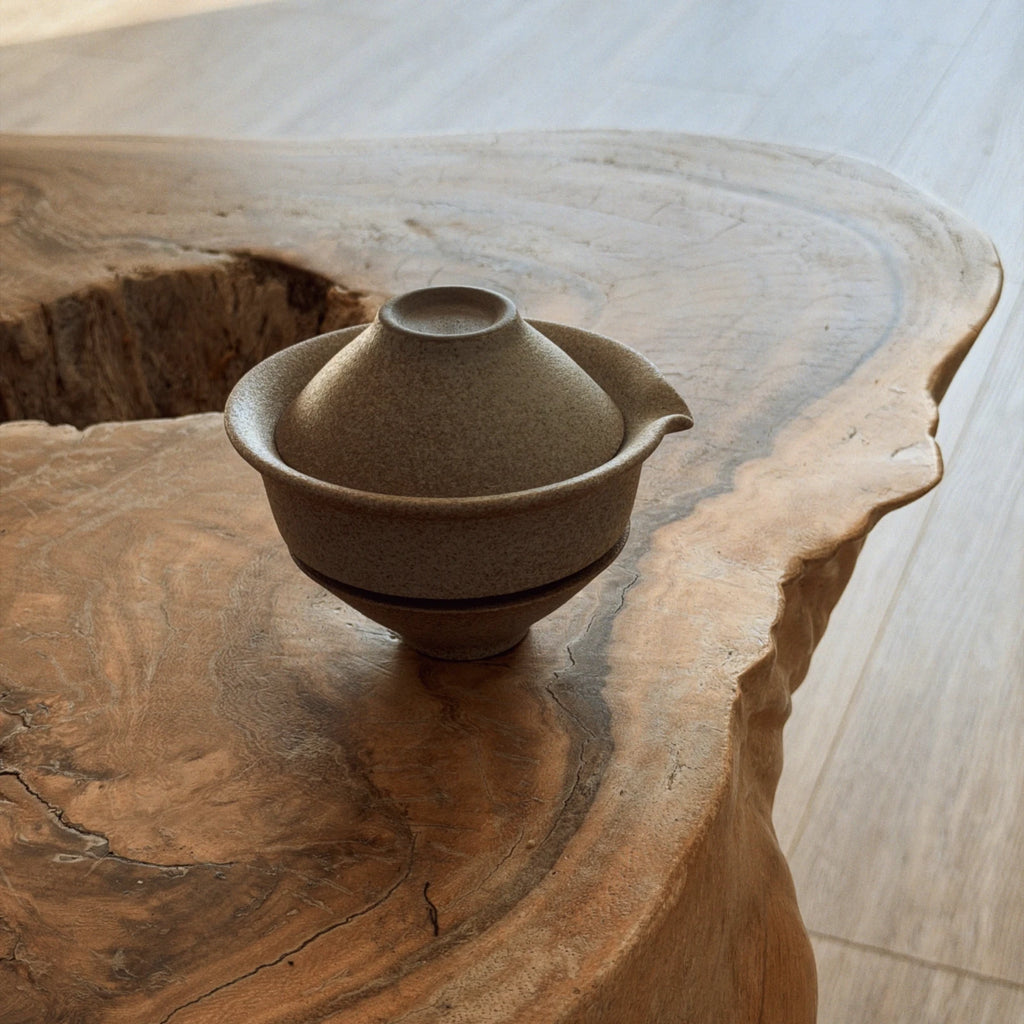 Beige ceramic gaiwan and two cups close-up view on natural wood slab