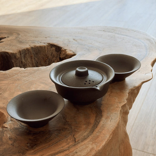 Dark ceramic gaiwan tea set with 2 cups on a natural live-edge wooden table