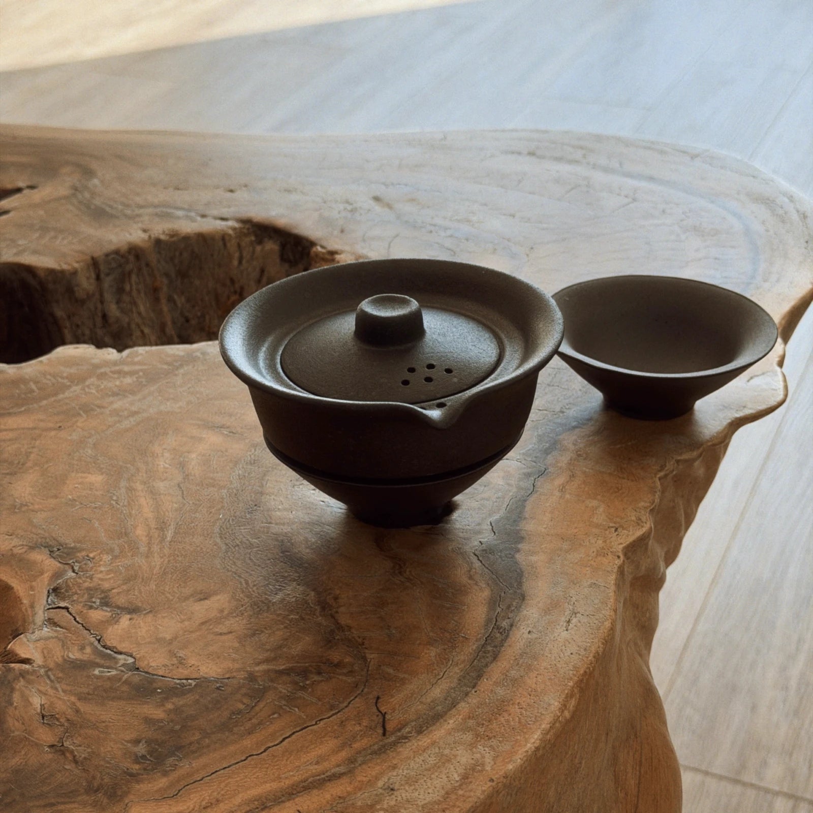 Dark ceramic gaiwan with closed lid and 2 cups arranged on rustic live-edge wood