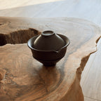 Side view of dark ceramic gaiwan tea set with 2 cups on natural wooden table