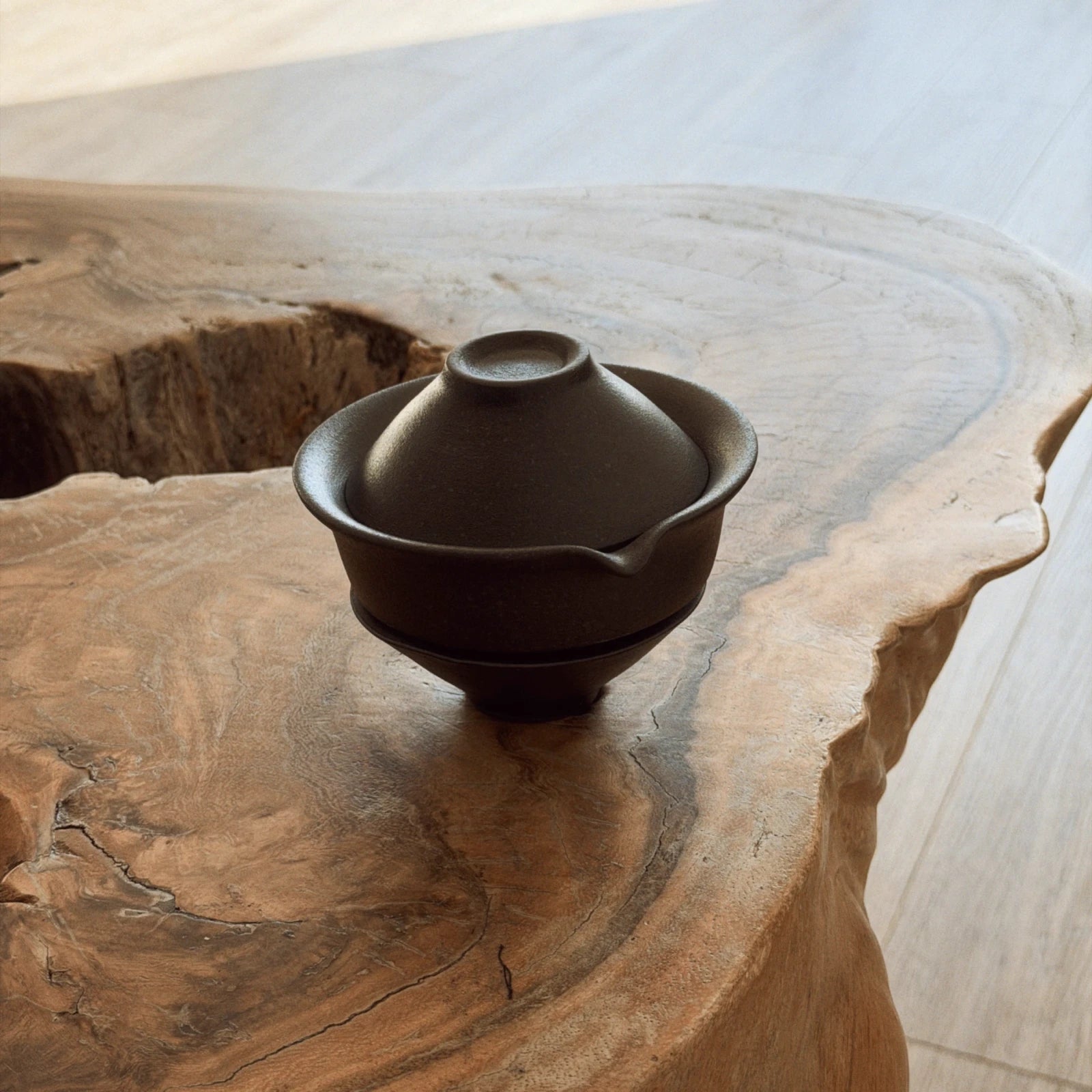 Side view of dark ceramic gaiwan tea set with 2 cups on natural wooden table